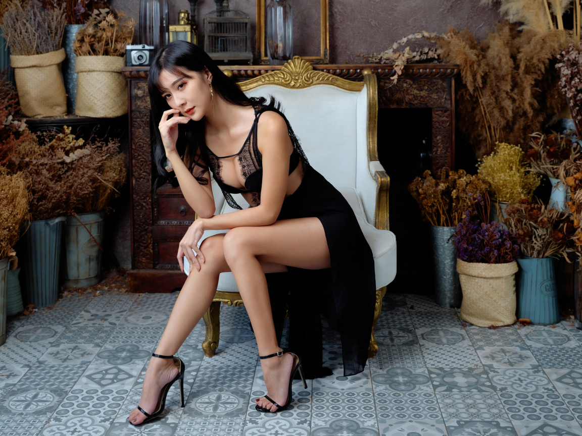 Красивая девушка азиатка в черном платье сидит в белом кресле 