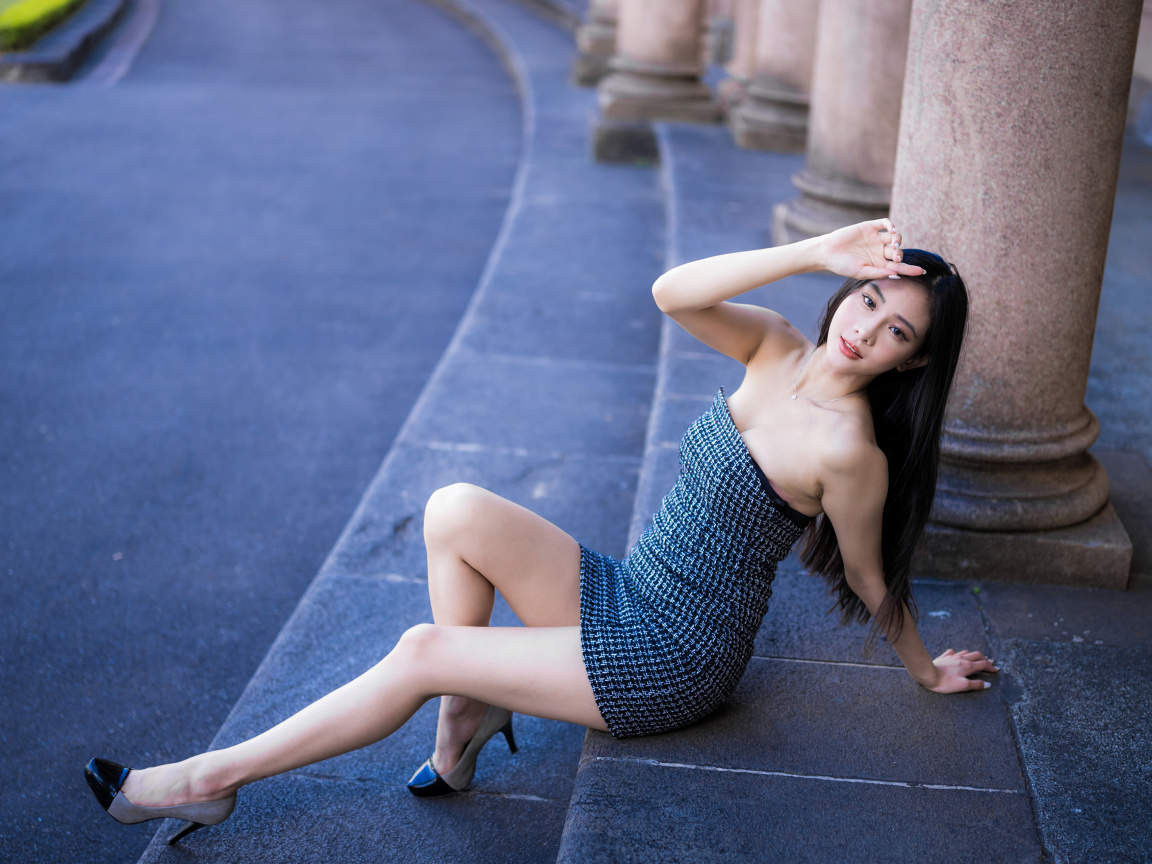 Красивая девушка азиатка в сером платье сидит на ступеньках