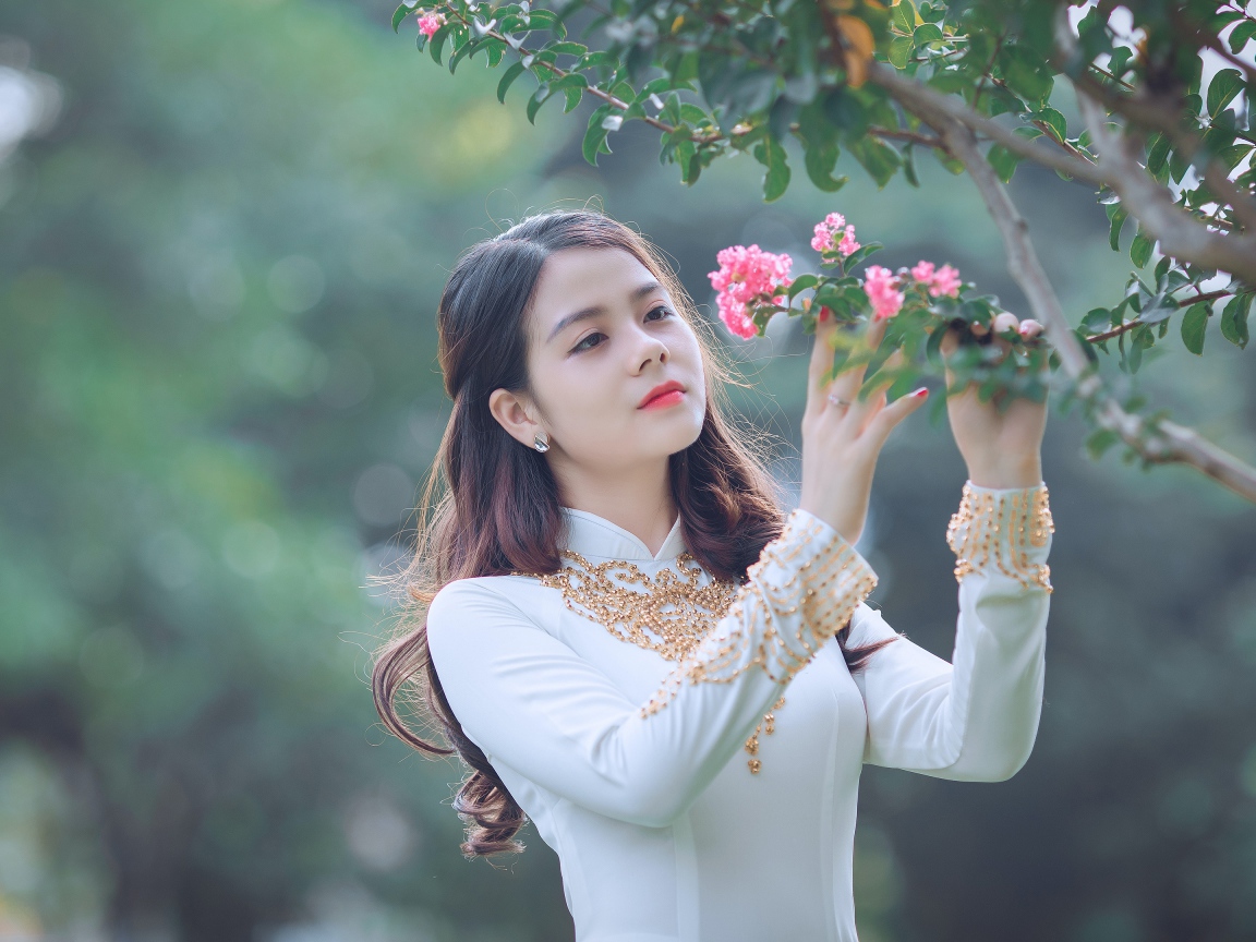 Красивая азиатка в белом платье у ветки с розовыми цветами