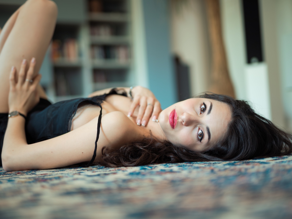 Красивая брюнетка в черном платье лежит на полу