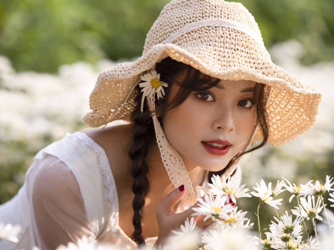 Красивая девушка в шляпе на поле с ромашками 