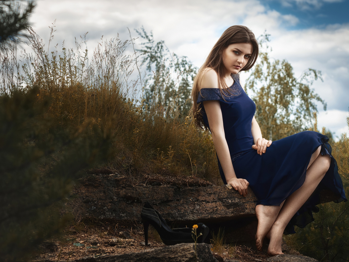 Красивая девушка в длинном синем платье сидит на камне 