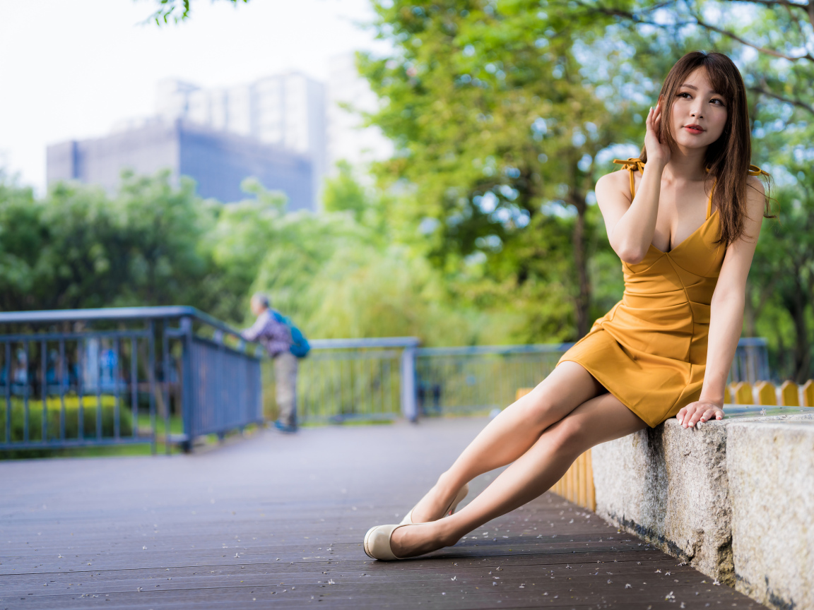 Красивая девушка в желтом платье сидит в парке 