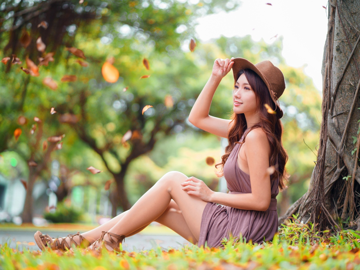 Веселая девушка азиатка сидит на земле в осеннем парке 