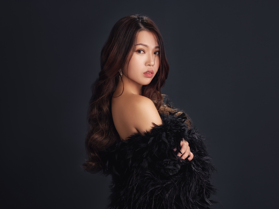 Милая девушка азиатка в черном наряде на сером фоне