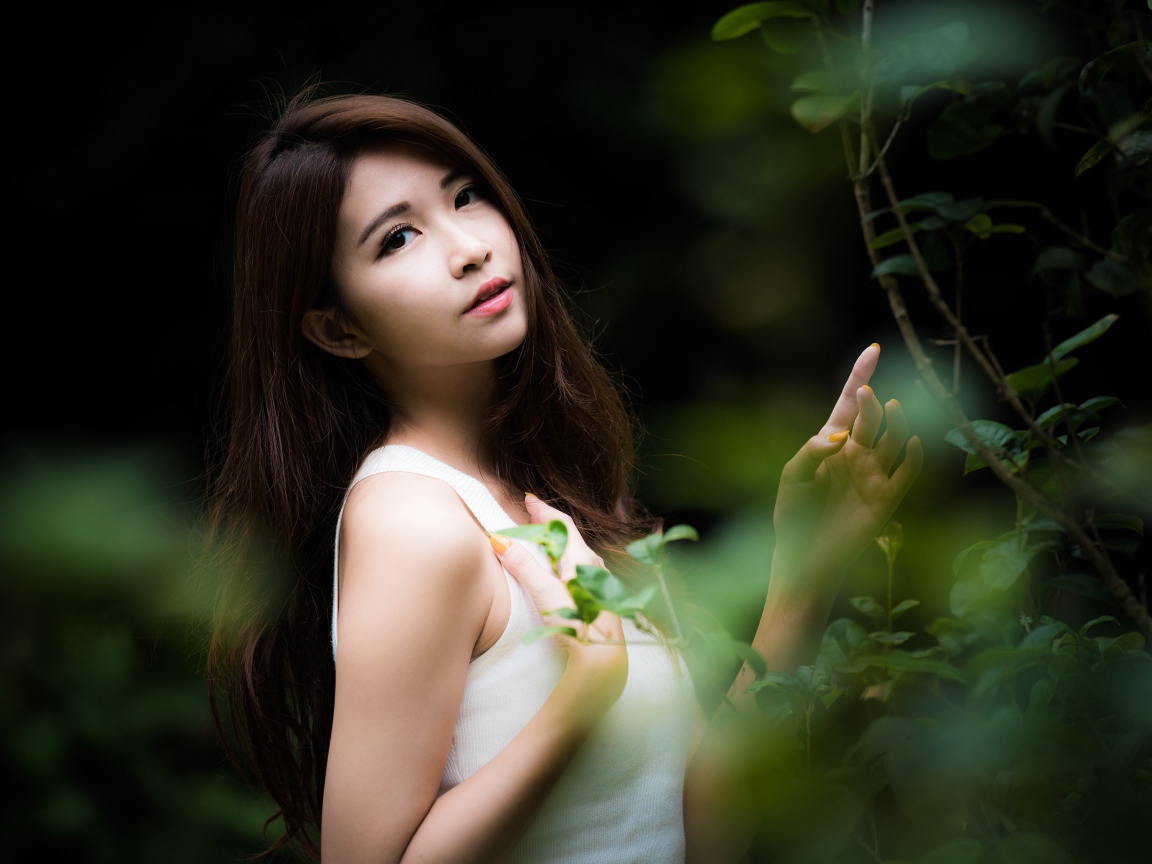 Милая азиатка в белом стоит у зеленых листьев