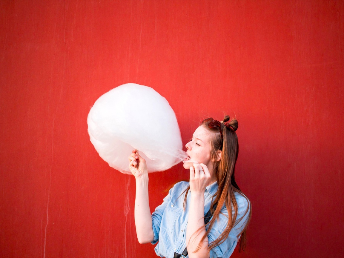 Девушка ест сладкую вату на красном фоне 