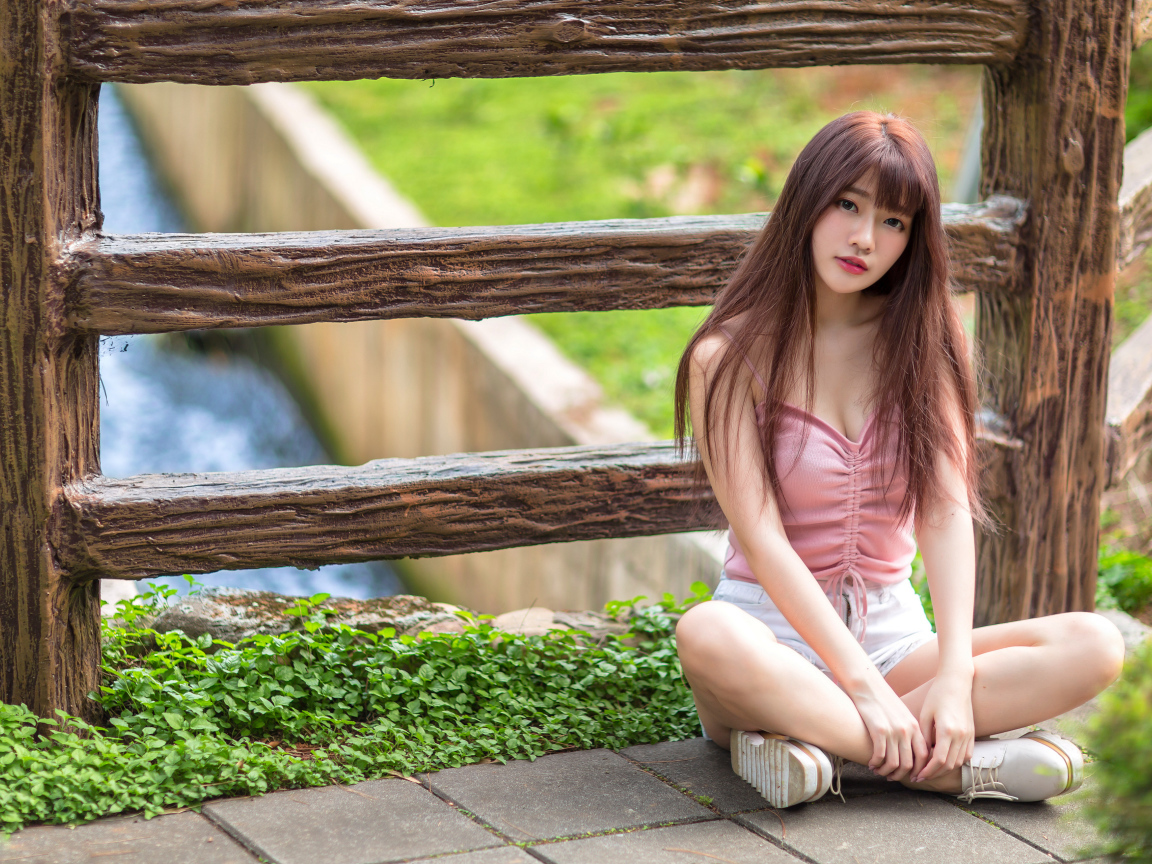 Длинноволосая азиатка сидит у забора 