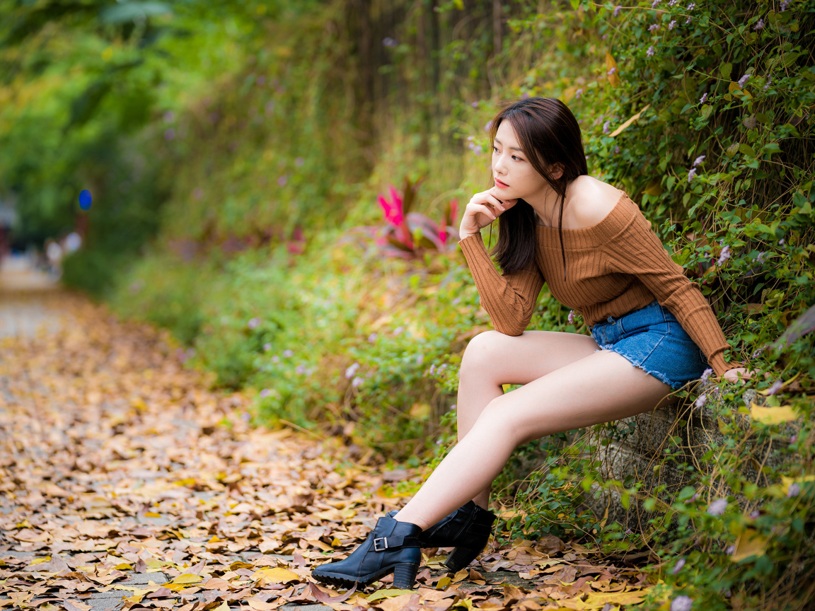 Задумчивая азиатка сидит в парке осенью 