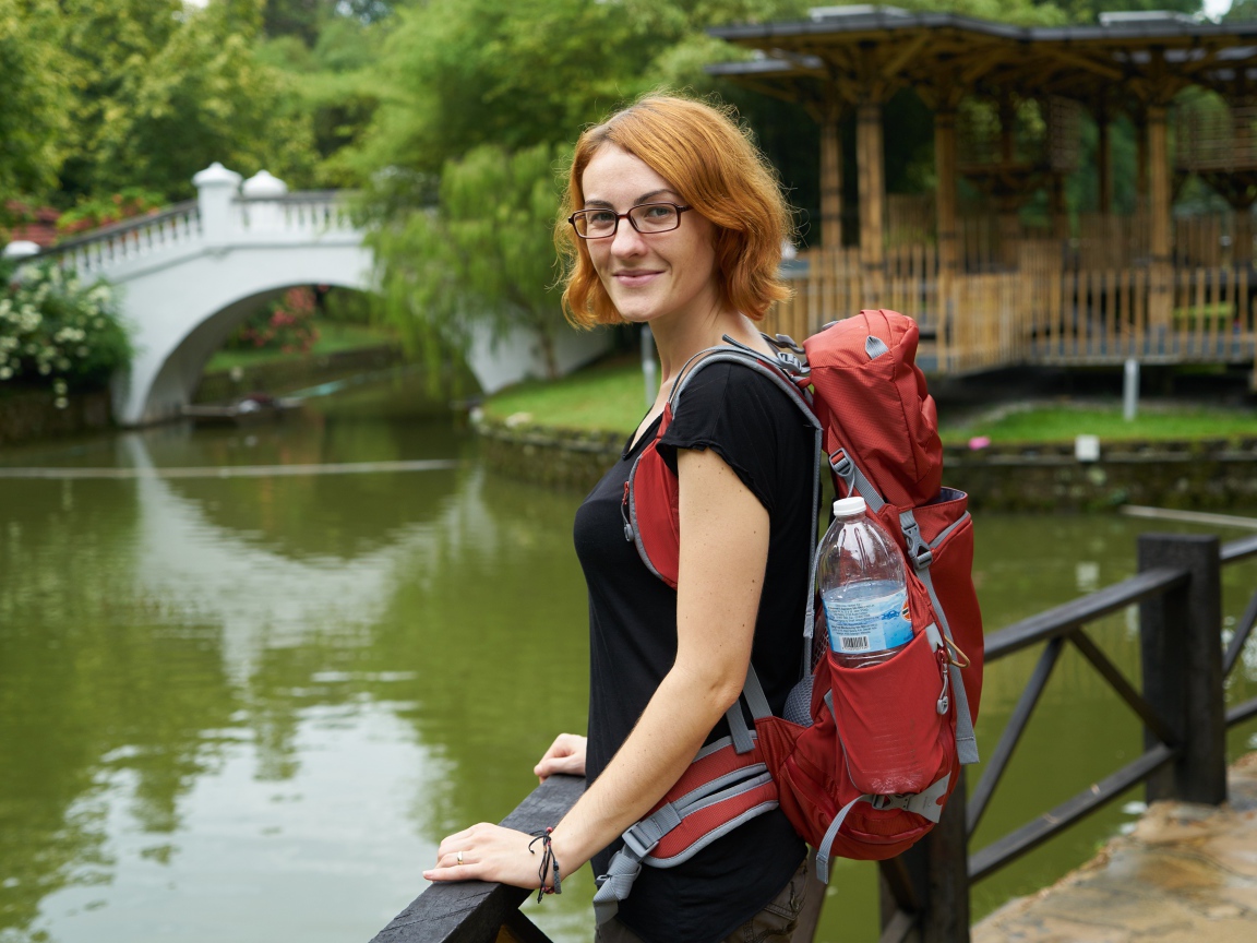 Рыжеволосая девушка с рюкзаком у пруда 