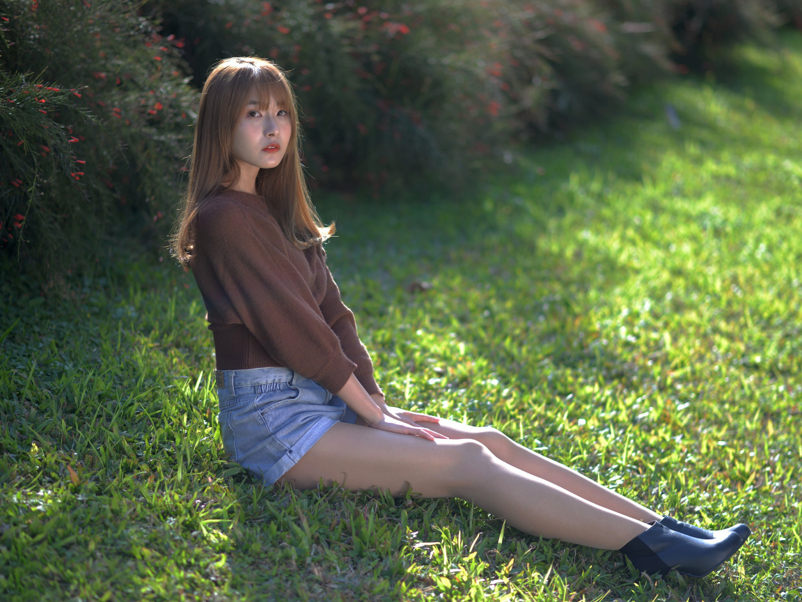 Грустная девушка азиатка сидит на зеленой траве 