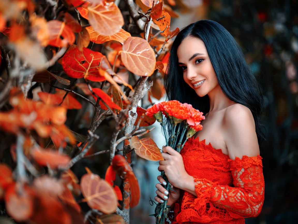Улыбающаяся девушка с букетом гвоздик у стены с осенними листьями