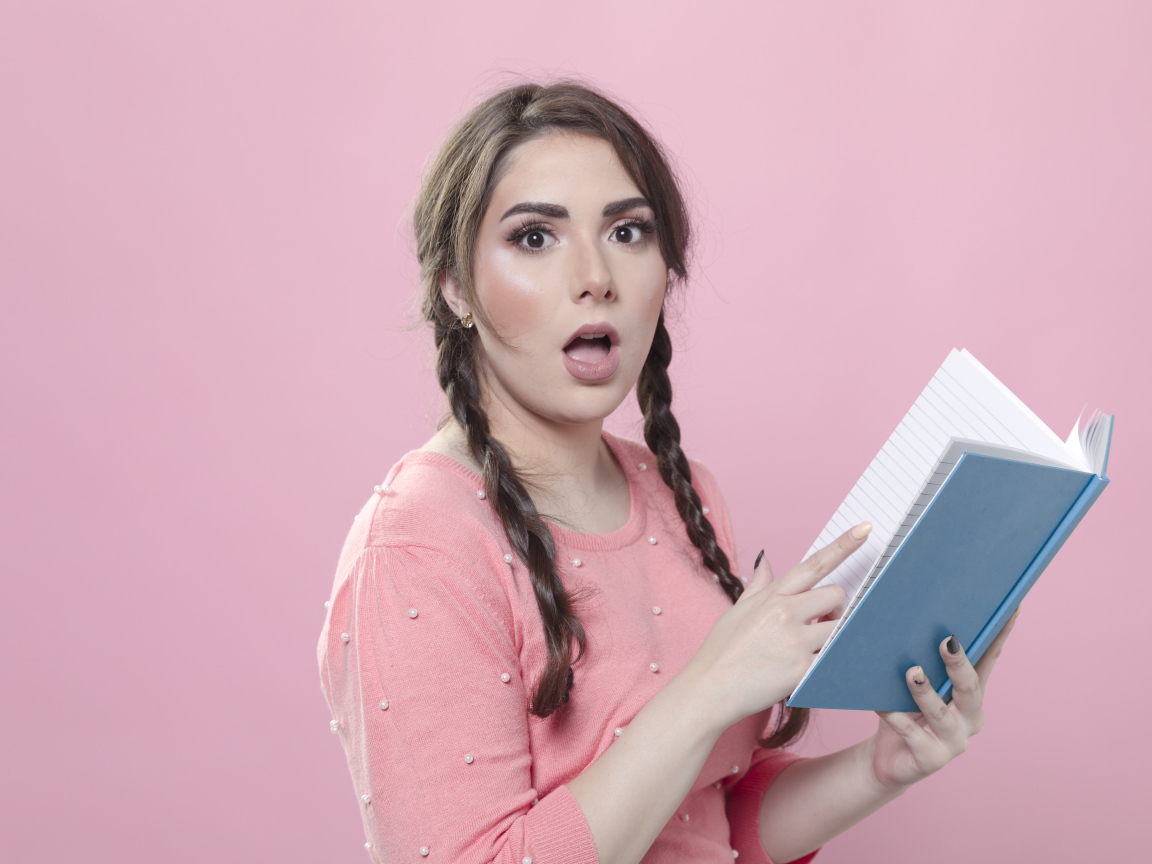 Удивленная девушка с книгой на розовом фоне
