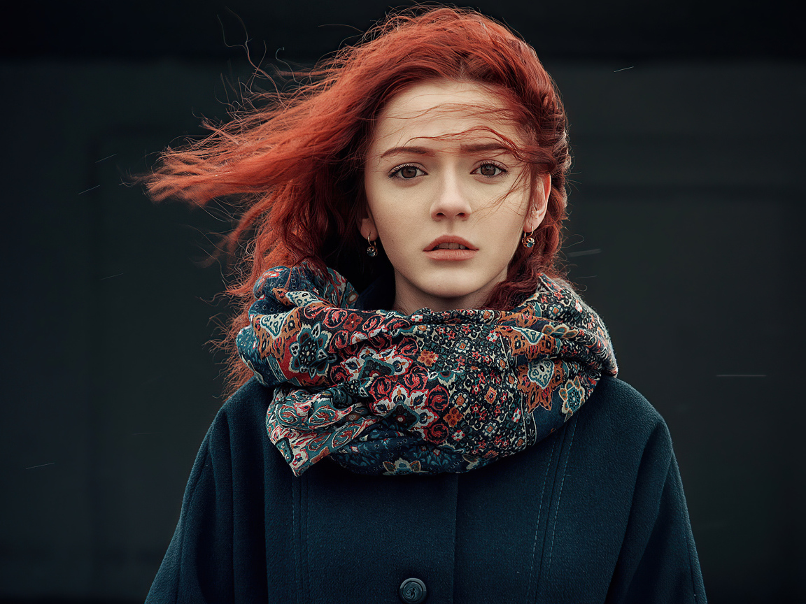 Ветер развивает волосы рыжеволосой девушки в пальто