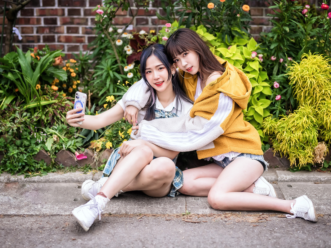 Две девушки азиатки сидят у стены с цветами 