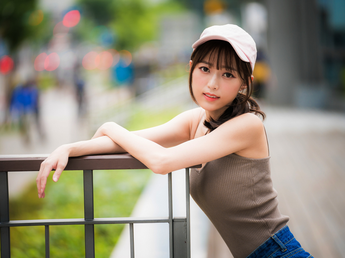 Молодая азиатка в кепке у перил 