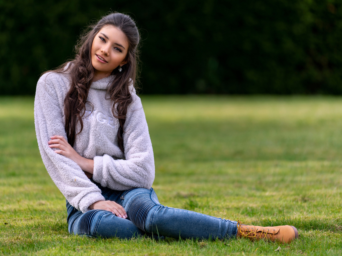 Молодая длинноволосая девушка сидит на траве 