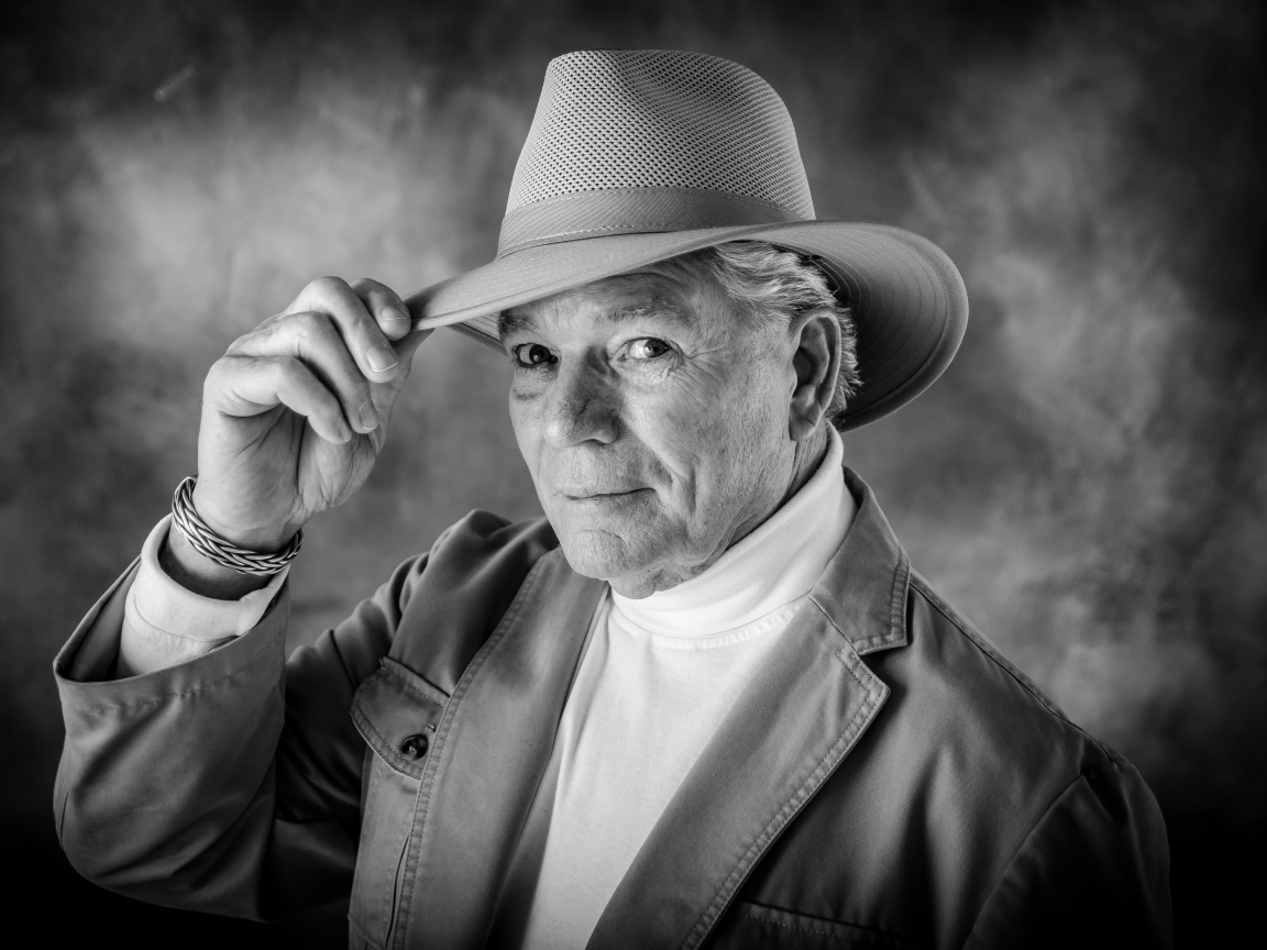 Пожилой мужчина в шляпе на фоне дыма 