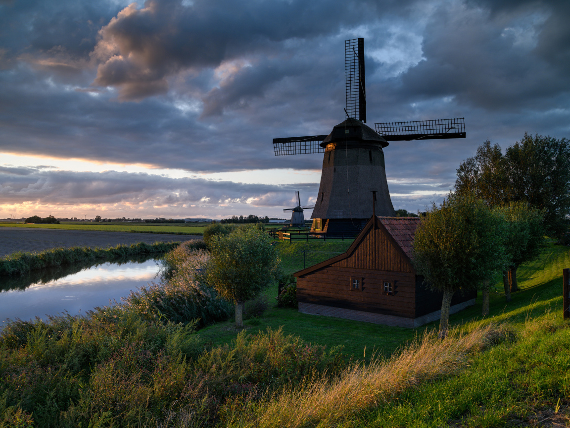 Большая ветряная мельница у реки на закате