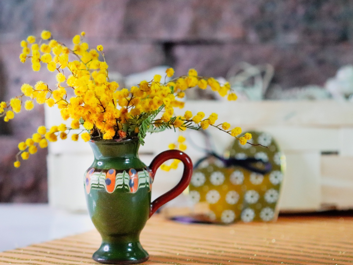 Желтые цветы мимозы в маленькой вазе на столе