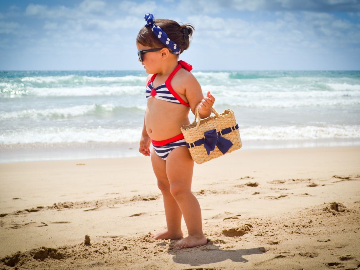 Маленькая девочка в купальнике гуляет по пляжу 