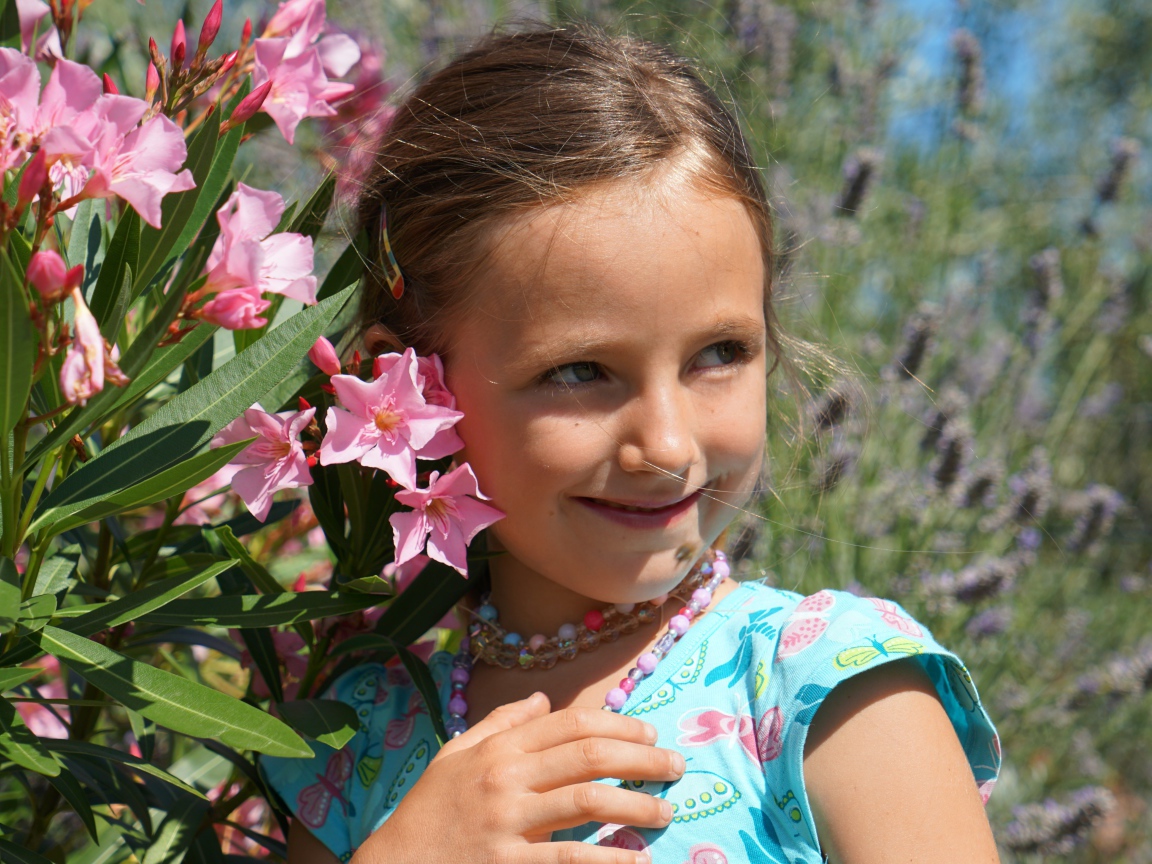 Маленькая девочка стоит у растения с розовыми цветами 