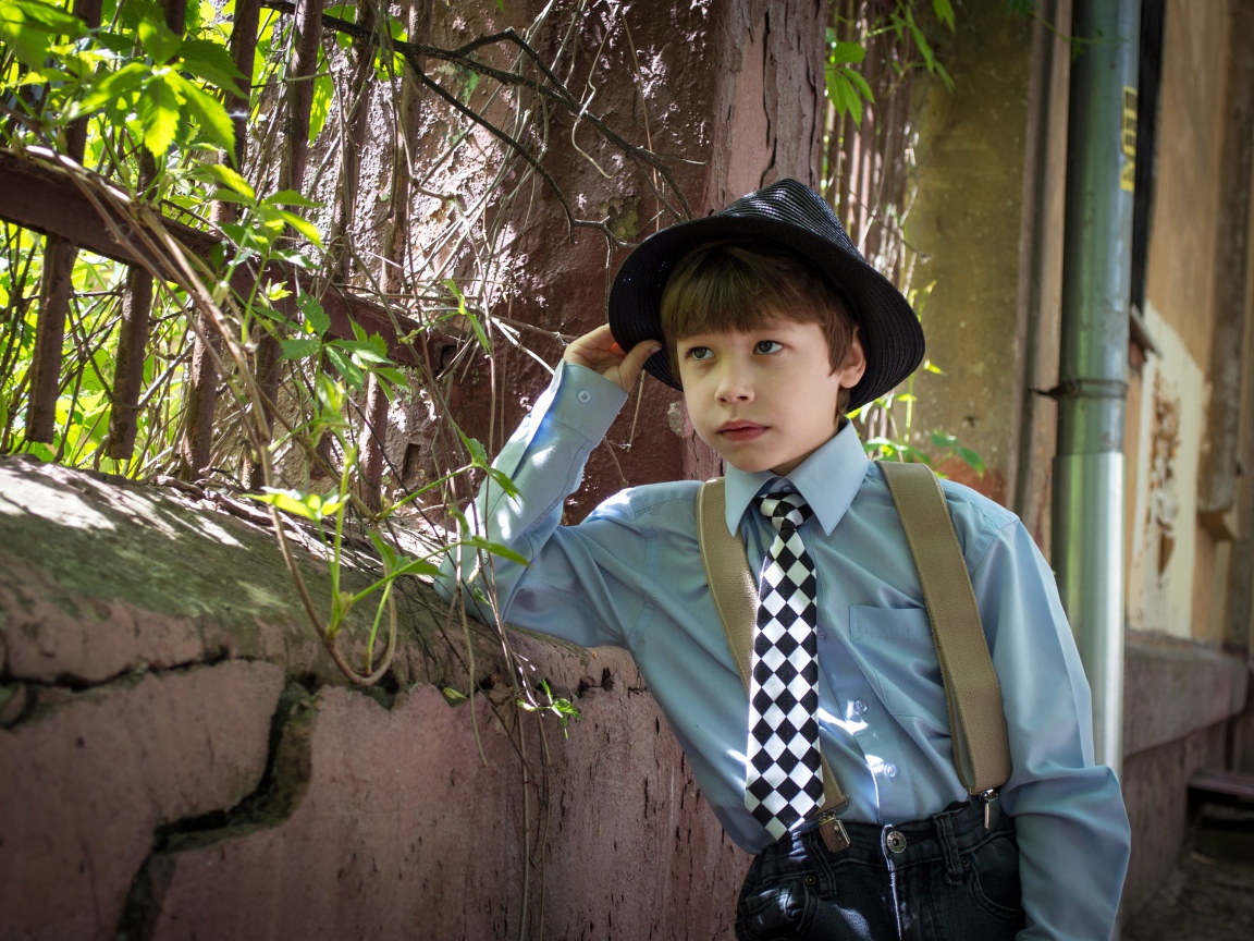 Красивый мальчик в шляпе стоит у забора 