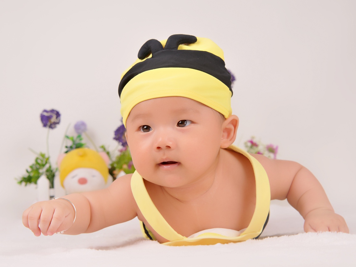 Маленький мальчик в шапке пчелы на сером фоне 