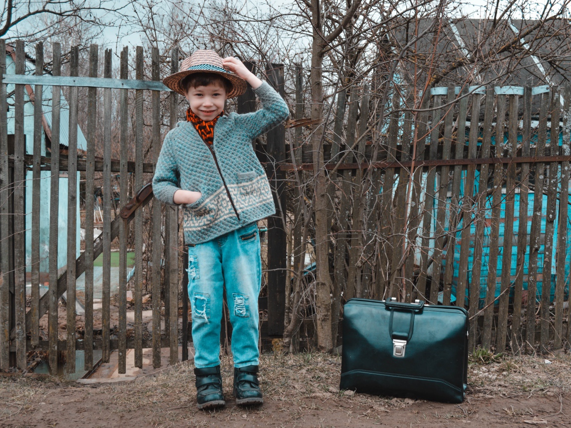 Маленький мальчик с чемоданом у забора