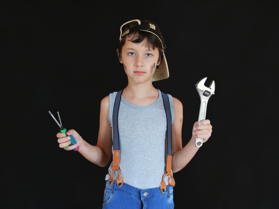 Маленький мальчик с инструментами в руках на черном фоне