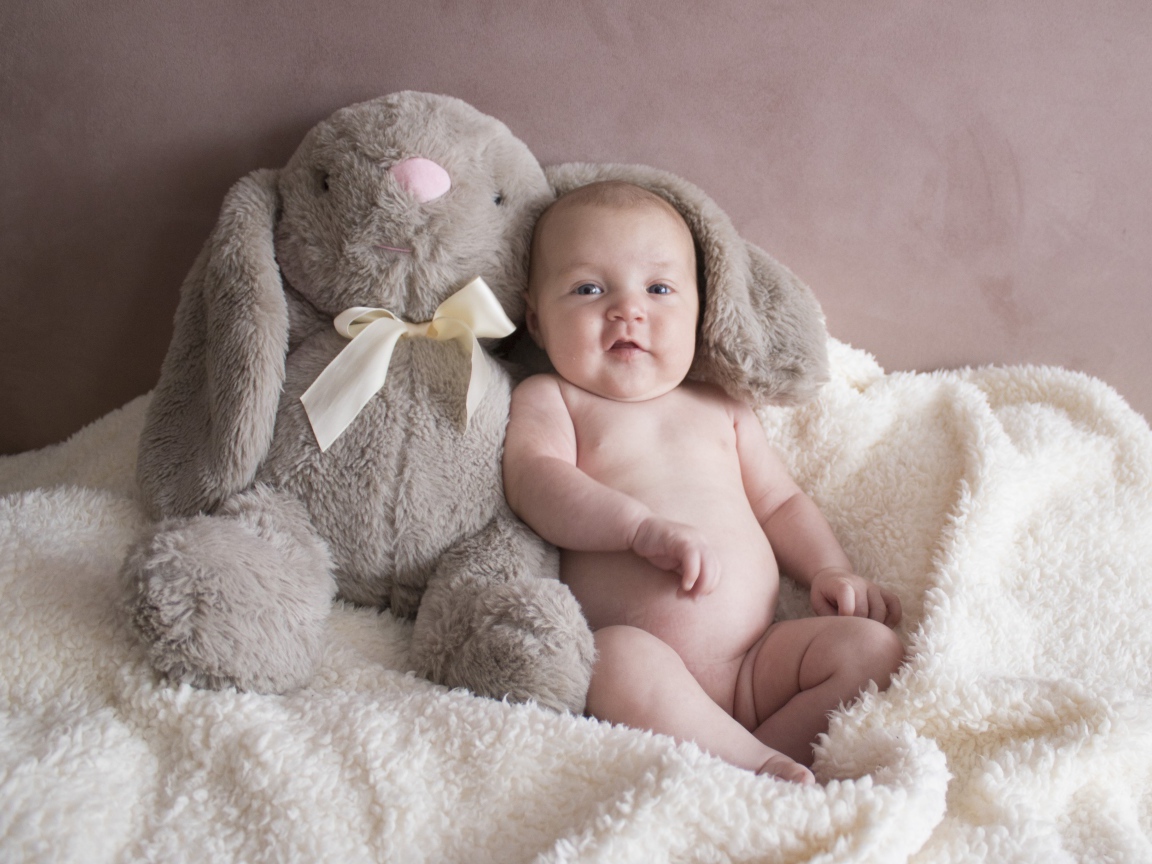 Маленький ребенок с игрушкой сидит у стены