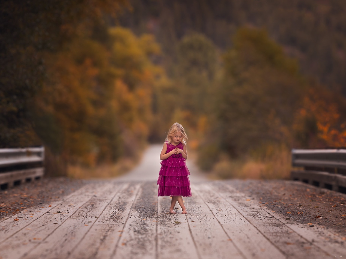 Маленькая девочка в платье стоит на мосту 