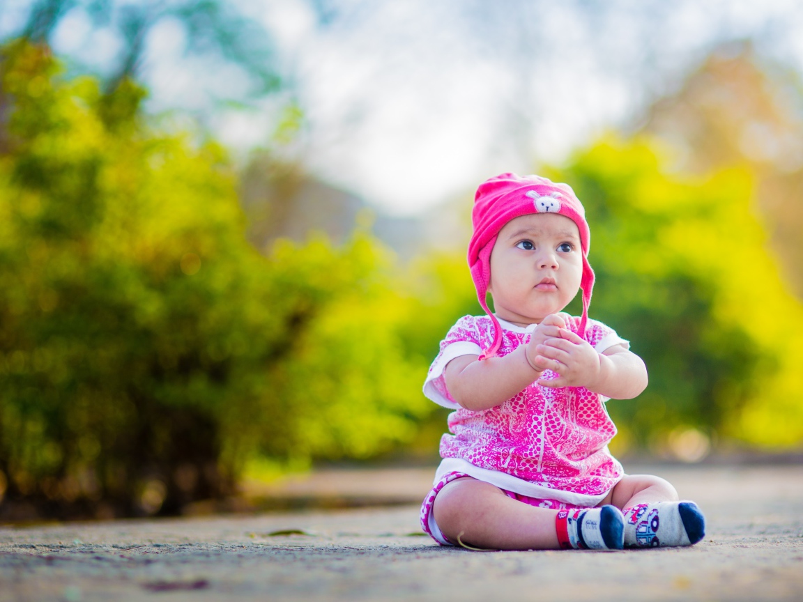 Маленькая девочка в розовом костюме сидит на земле