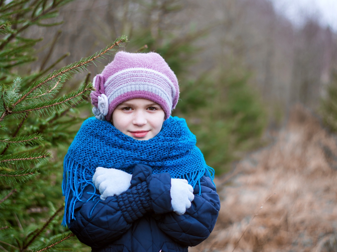 Маленькая девочка в теплой одежде у ели