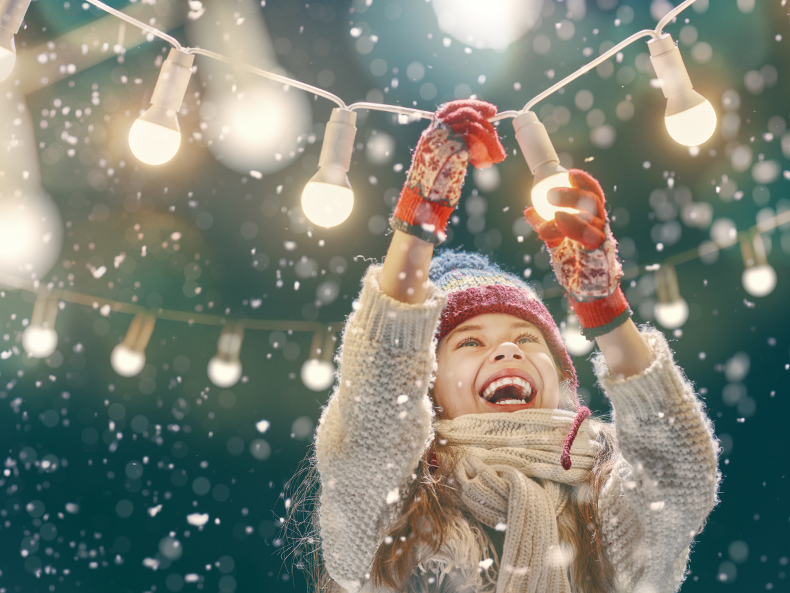 Улыбающаяся девочка вешает лампочки 