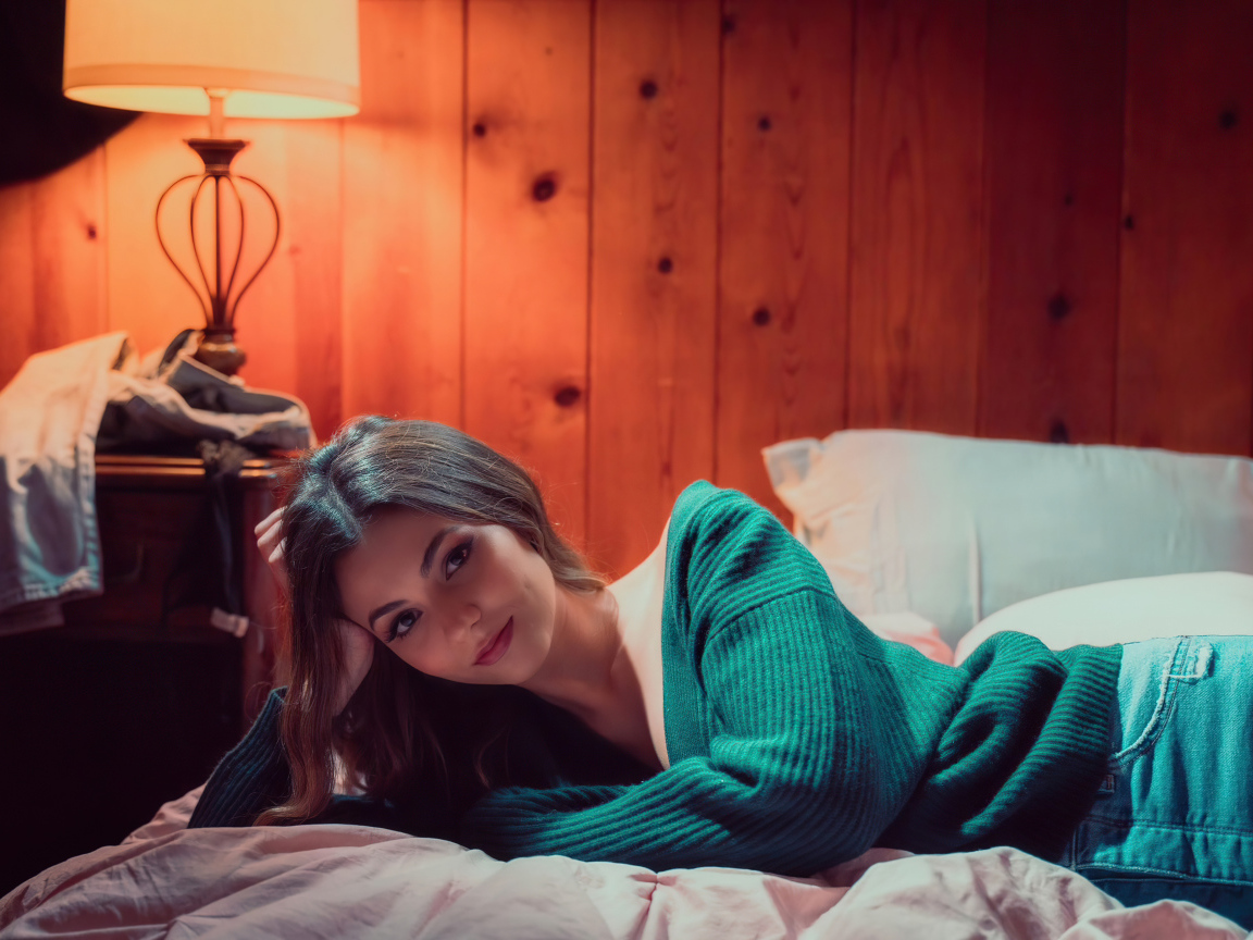 Актриса  Виктория Джастис в зеленом свитере на кровати