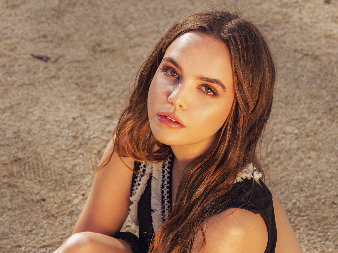 Кареглазая актриса Бэйли Мэдисон сидит на песке