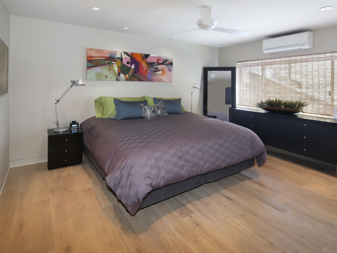 Большая серая кровать в спальне с белыми стенами