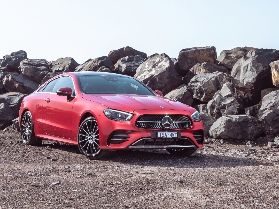 Красный автомобиль Mercedes-Benz E 350 AMG Line Coupé 2023 года у камней