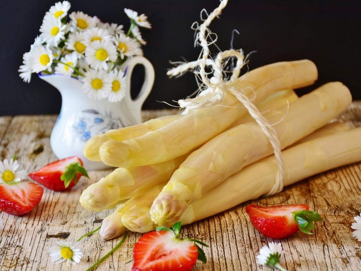 Спаржа на столе с ромашками и ягодами клубники