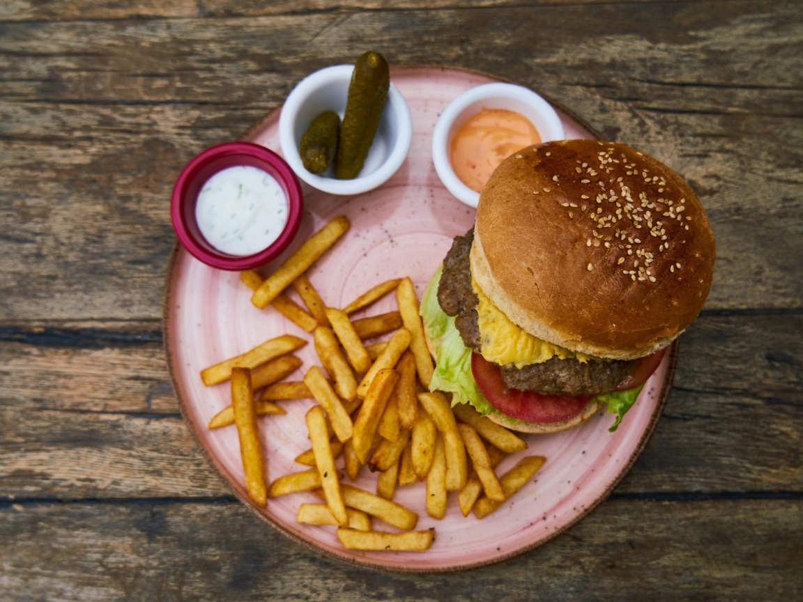 Гамбургер на тарелке с картофелем фри, огурцами и соусом