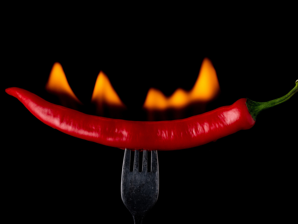 Жгучий красный перец на вилке на черном фоне