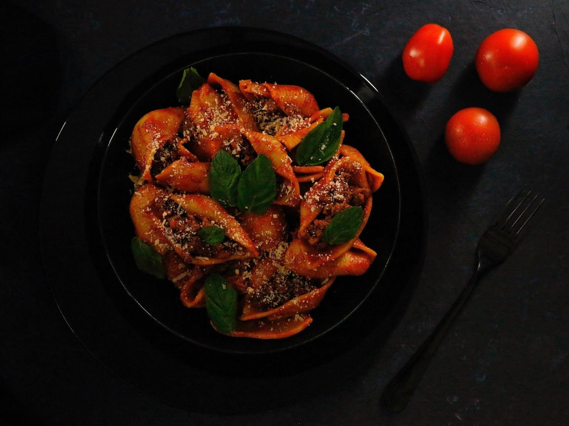 Большие макароны с фаршем в черной тарелке