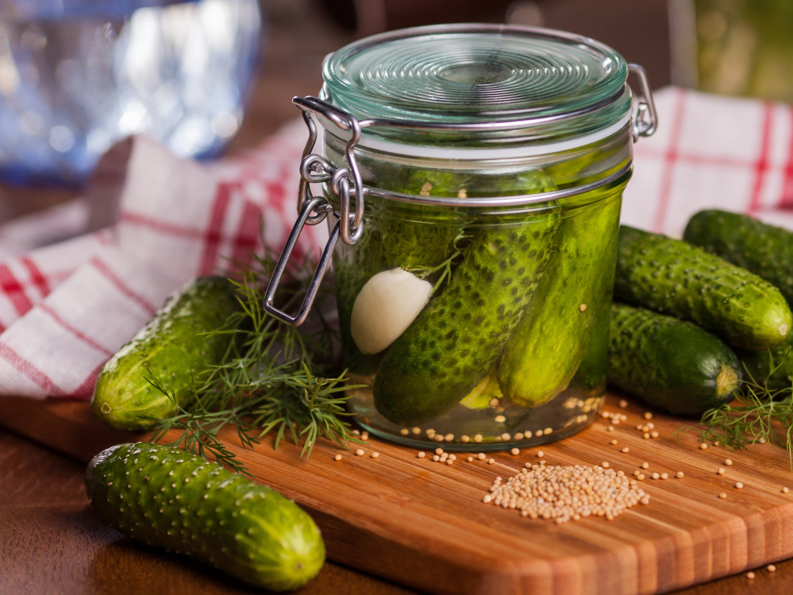 Маринованные огурцы в банке на столе со свежими