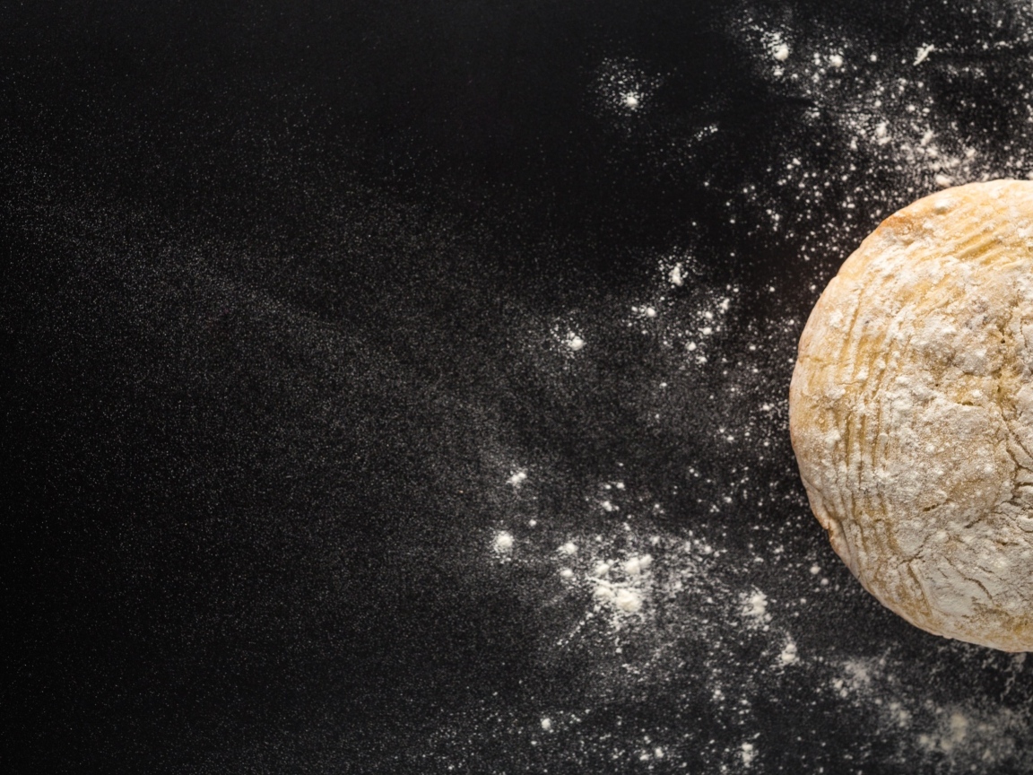 Сырое тесто на черном столе с мукой