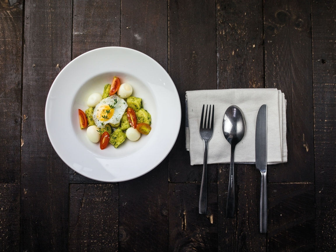 Яичница с овощами в белой тарелке на столе со столовыми приборами