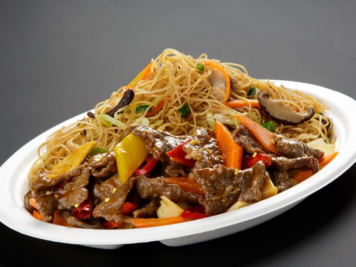 Острая лапша с грибами на белой тарелке на сером фоне