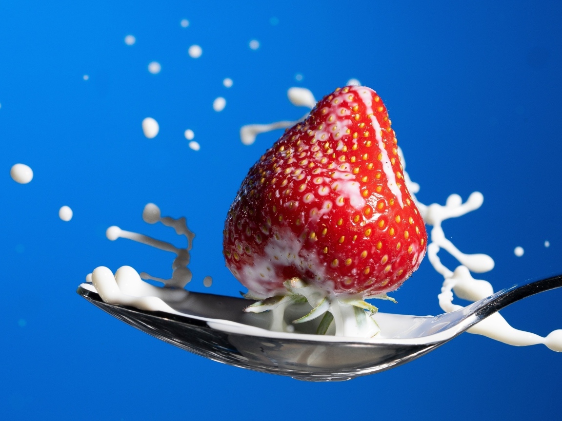 Молоко в ложке с клубникой на синем фоне