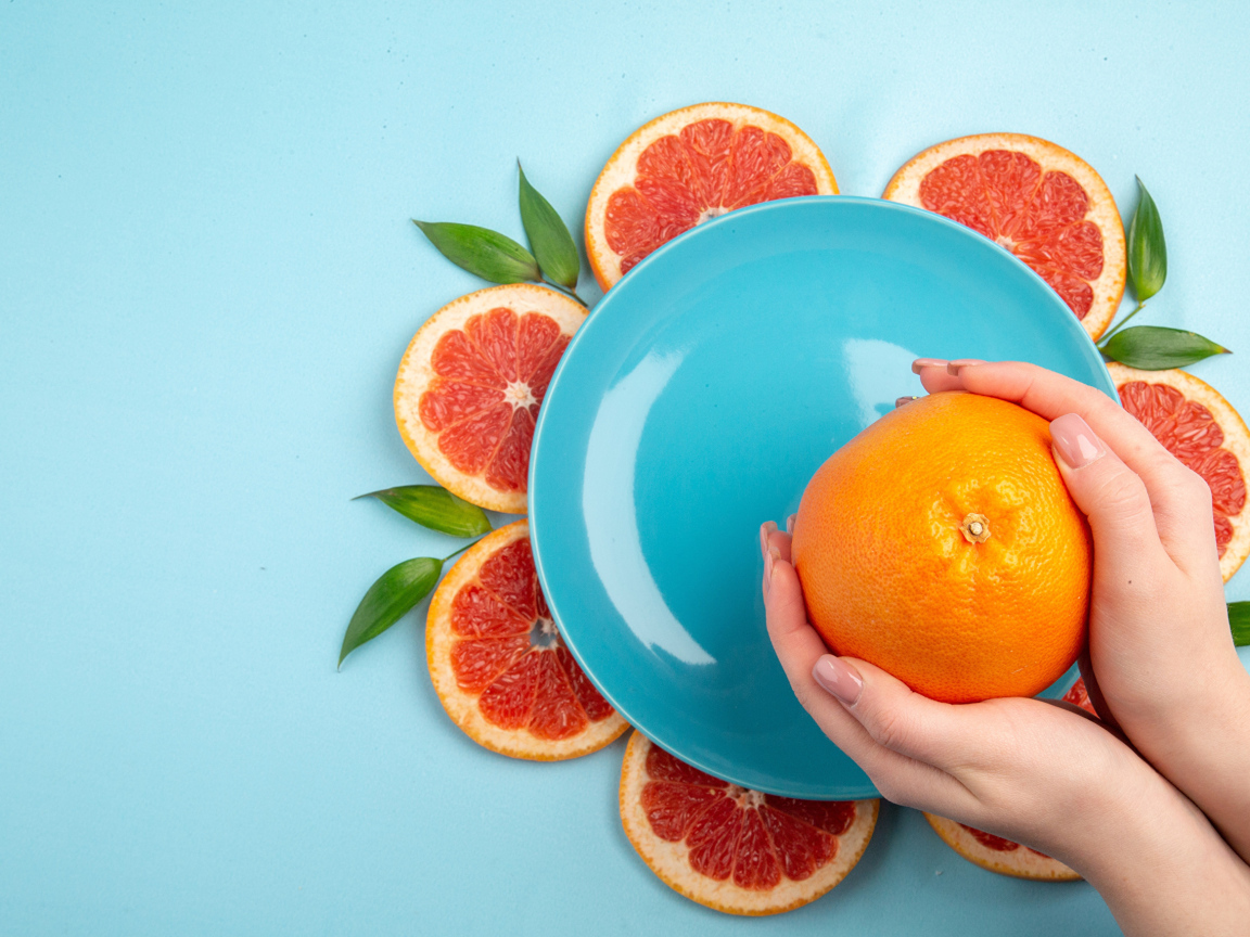 Апельсин в руках девушки на голубом фоне с тарелкой