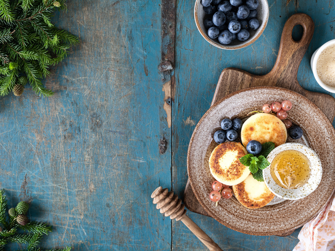 Сырники с ягодами черники на тарелке с медом